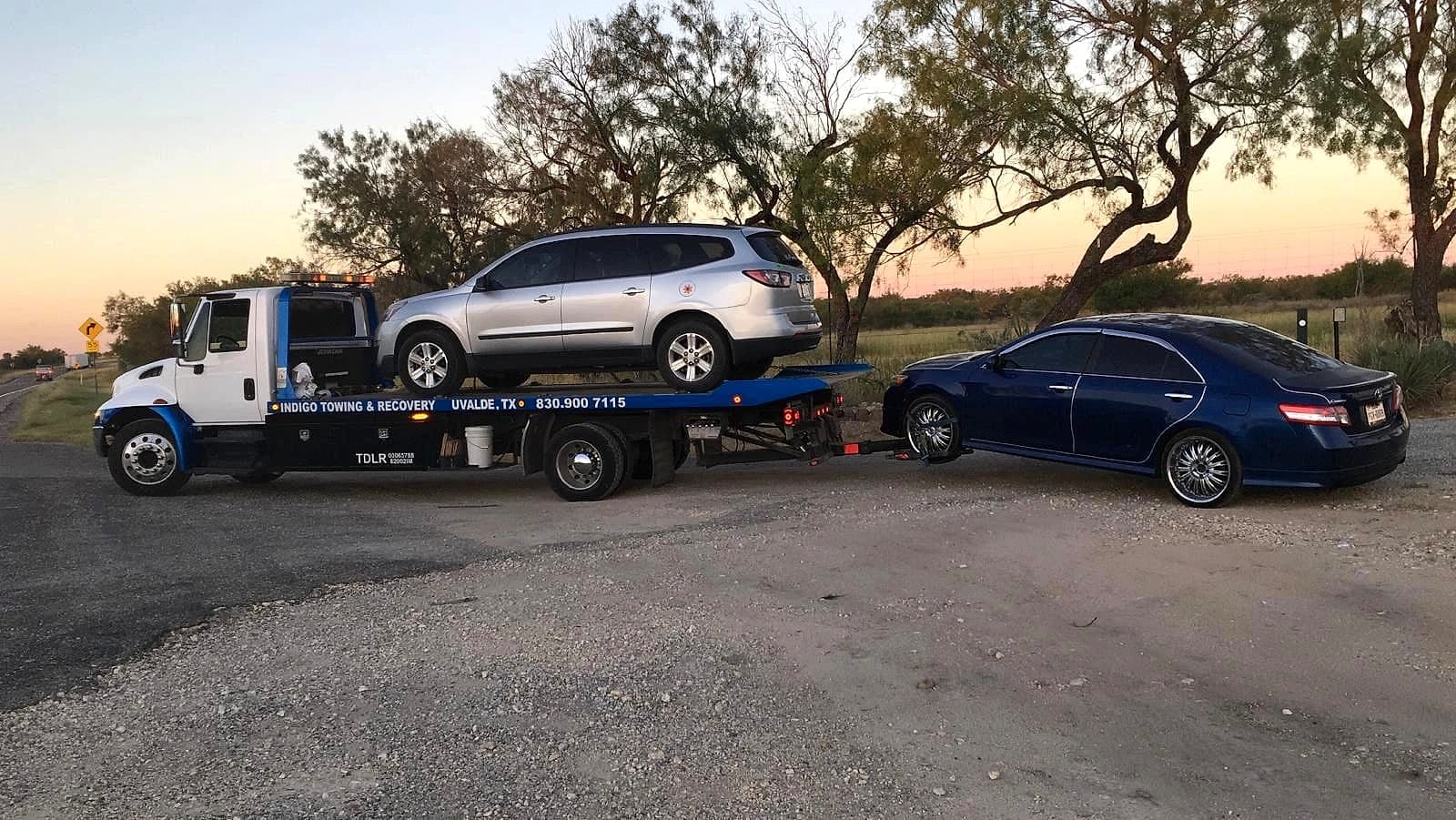Indigo Towing & Recovery flatbed hauling an SUV and towing a sedan at sunset near Uvalde, Texas